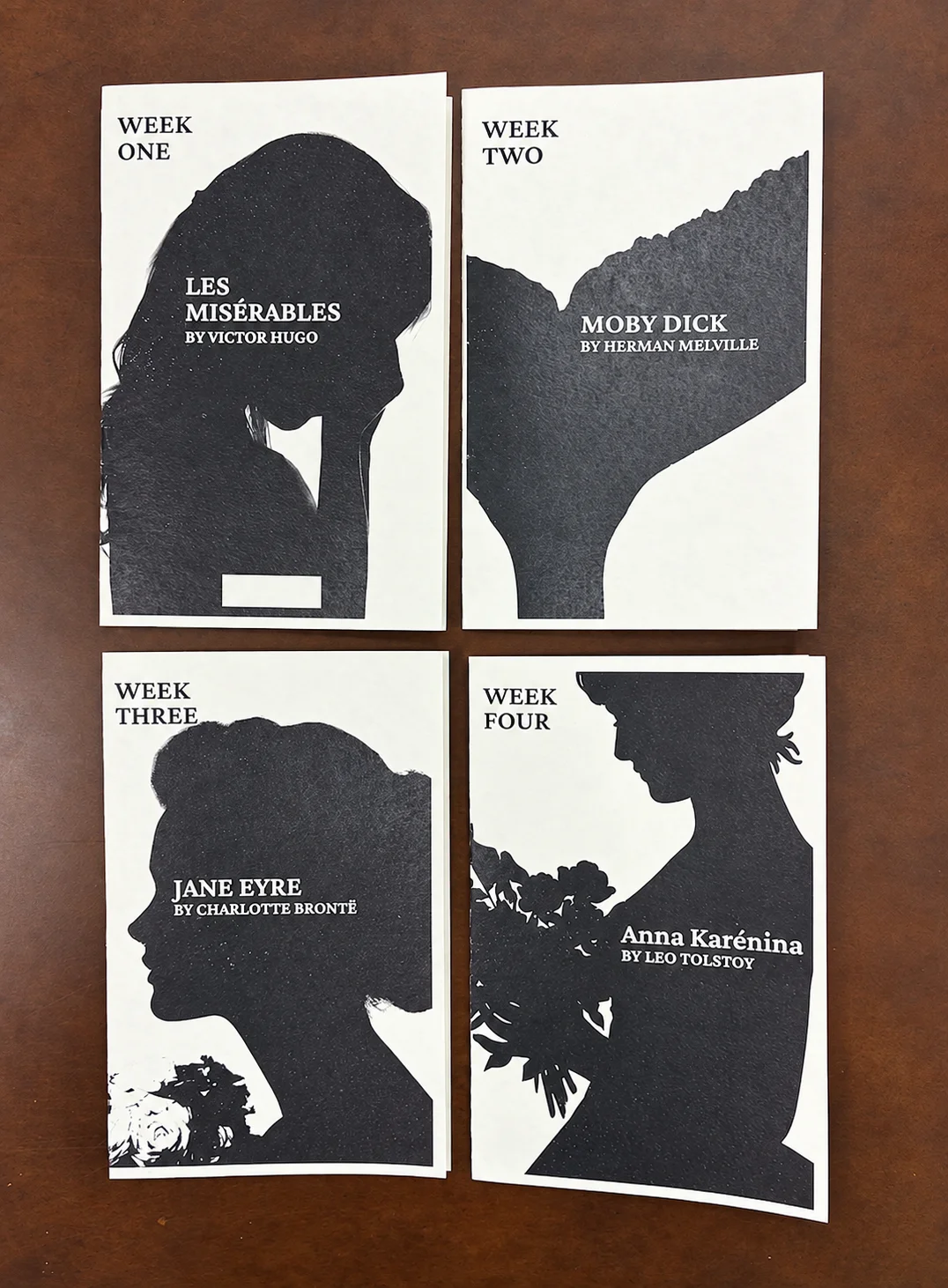 Four weekly Human by Hand packets arranged on a wooden table: Week One Les Misérables, Week Two Moby Dick, Week Three Jane Eyre, and Week Four Anna Karenina
