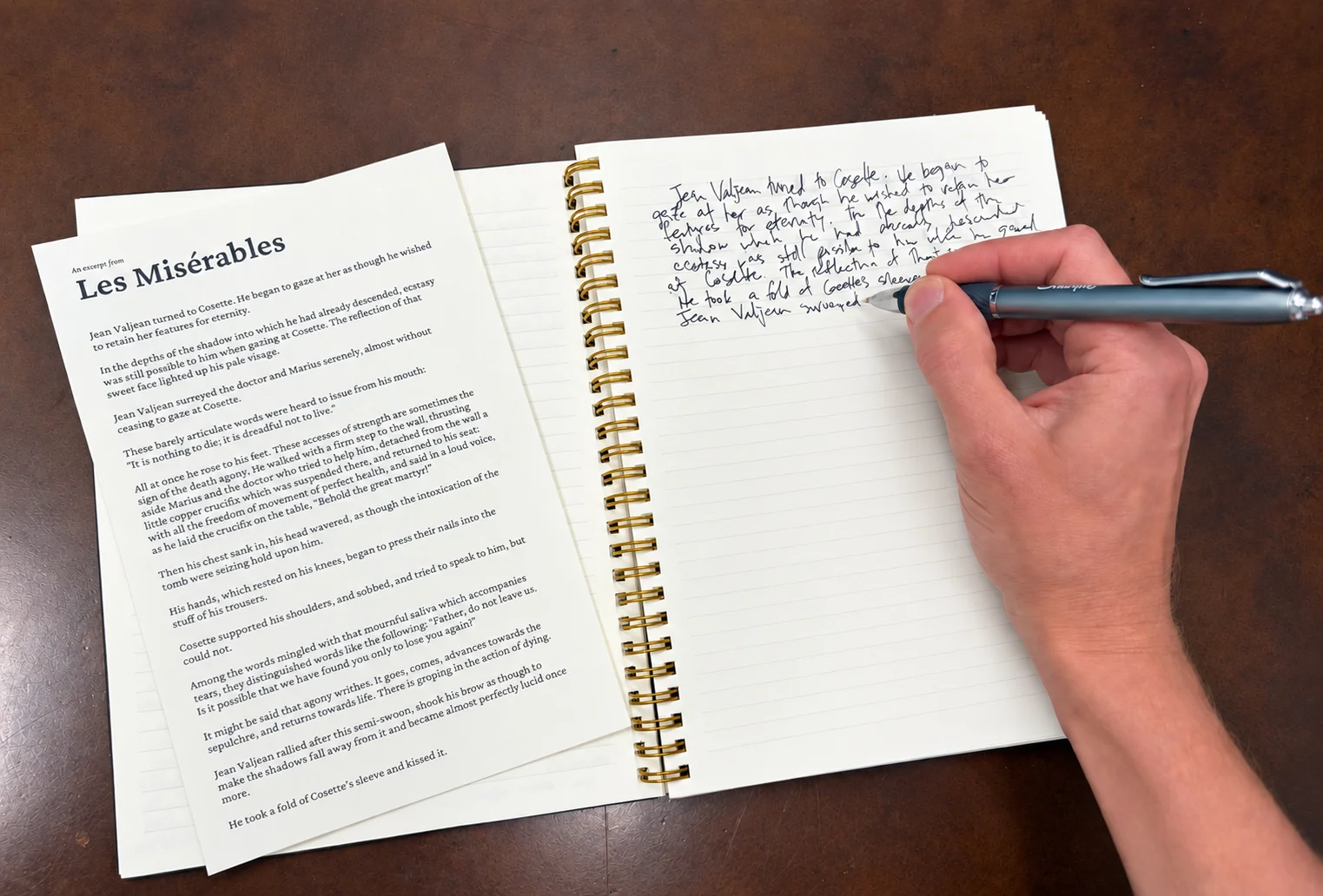 A hand copying an excerpt from Les Misérables into a spiral notebook beside the printed packet